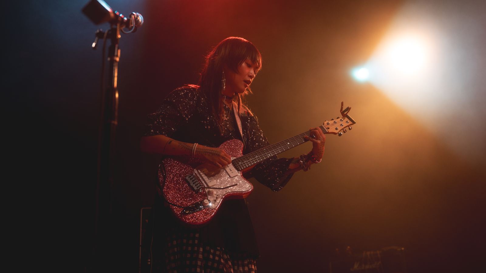 Yvette Young playing a glittery pink guitar onstage in a warm spotlight